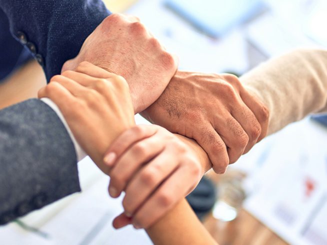 A close-up of four hands interlocked, symbolizing teamwork and strong IT partnerships for business success.